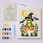 Frog Witch on a Toadstool canvas before and after punching, with the threads and tools