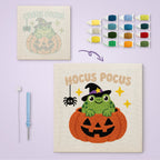Hocus Pocus Frog canvas before and after punching, with the threads and tools