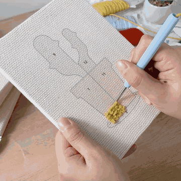 Hands punching a mini canvas with the punch needle