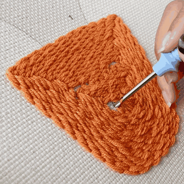 Hands punching a framed canvas with the punch needle