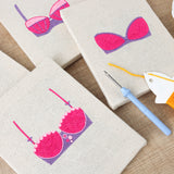 The four Pretty Pink Bras mini canvases on a wall above a shelf