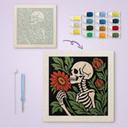 Skeleton Smelling a Flower canvas before and after punching, with the threads and tools